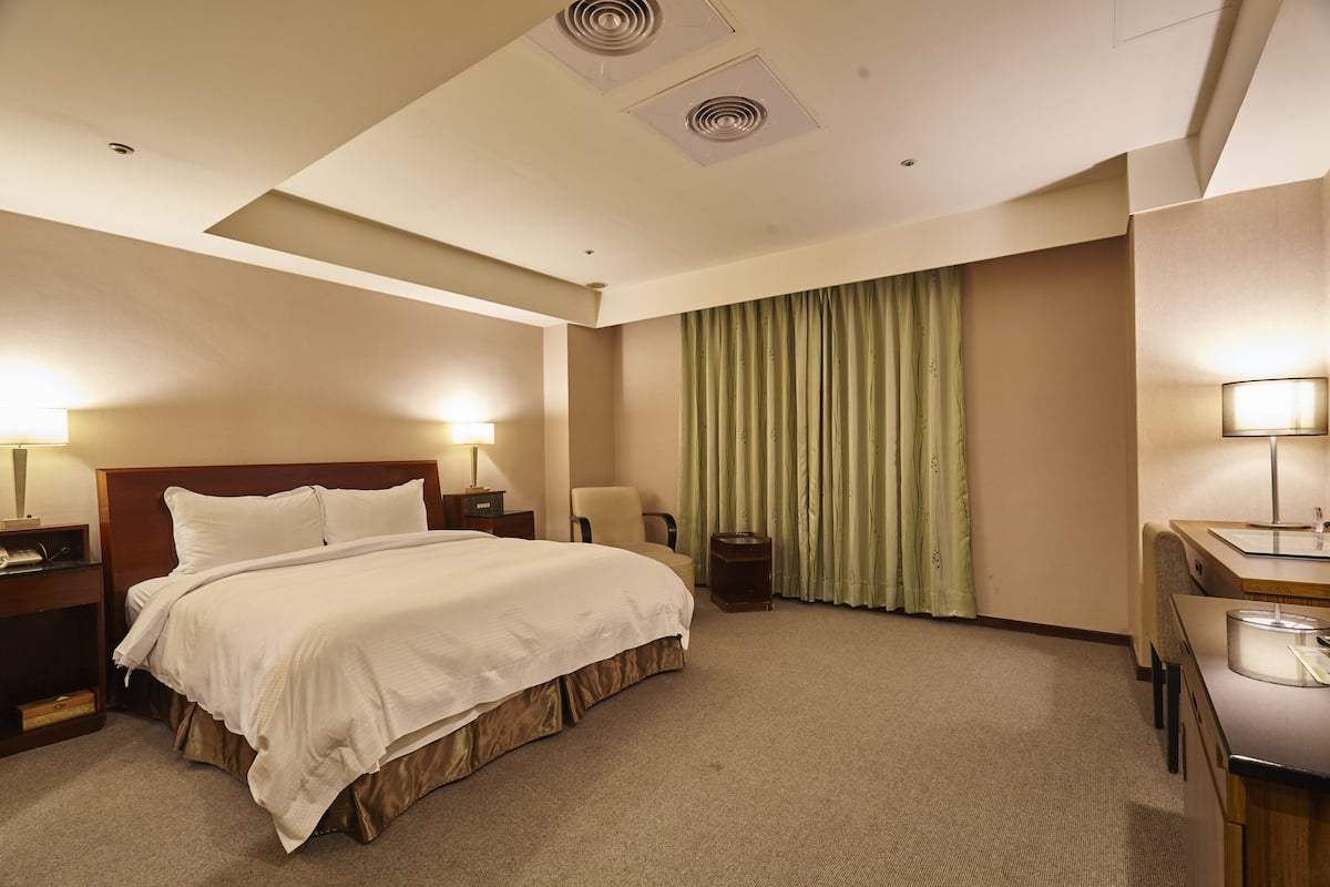 A hotel room with a large bed, bedside tables, a desk, and a chair.