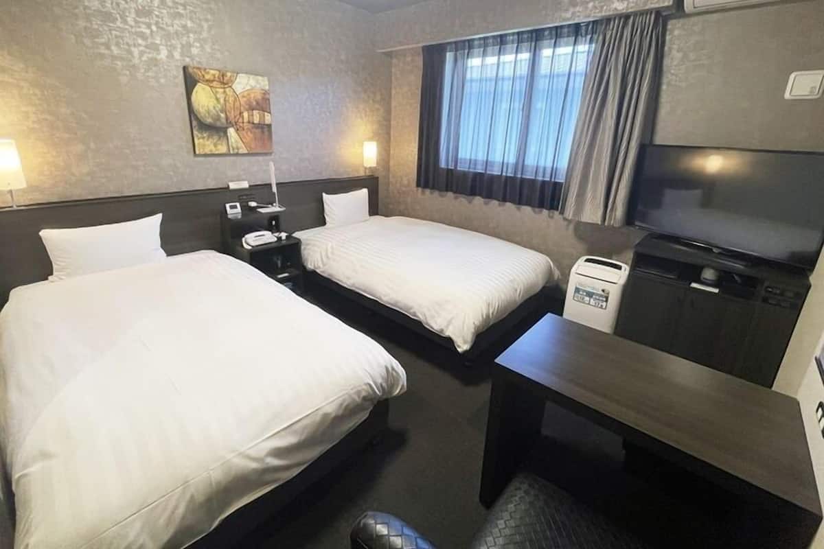 A hotel room with two beds, a desk, a TV, and a window with curtains.