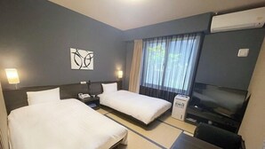 Habitación de hotel con dos camas, un escritorio, una silla, un televisor y una ventana con cortinas.