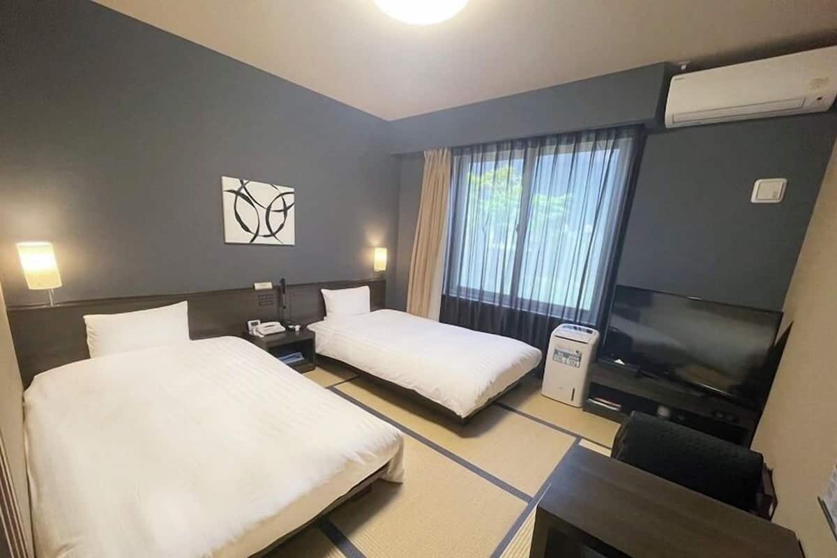 A hotel room with two beds, a desk, a chair, a TV, and a window with curtains.