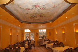 Uma sala de jantar com mesas e cadeiras, teto decorativo e vista pela janela.