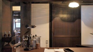 A wooden counter with a lamp, a book, and a smartphone. There are bottles and a kettle on the counter. - Sun & Moon Club (Fujinomiya)