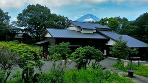 A building with a sloped roof, surrounded by lush greenery and a mountain in the background. - Sun & Moon Club (Fujinomiya)
