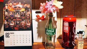 A calendar, a Coca-Cola bottle, a Coca-Cola can, and a Jack Daniel's bottle on a wooden surface. - SunCheon Guest House ChuChun - Hostel (Suncheon)