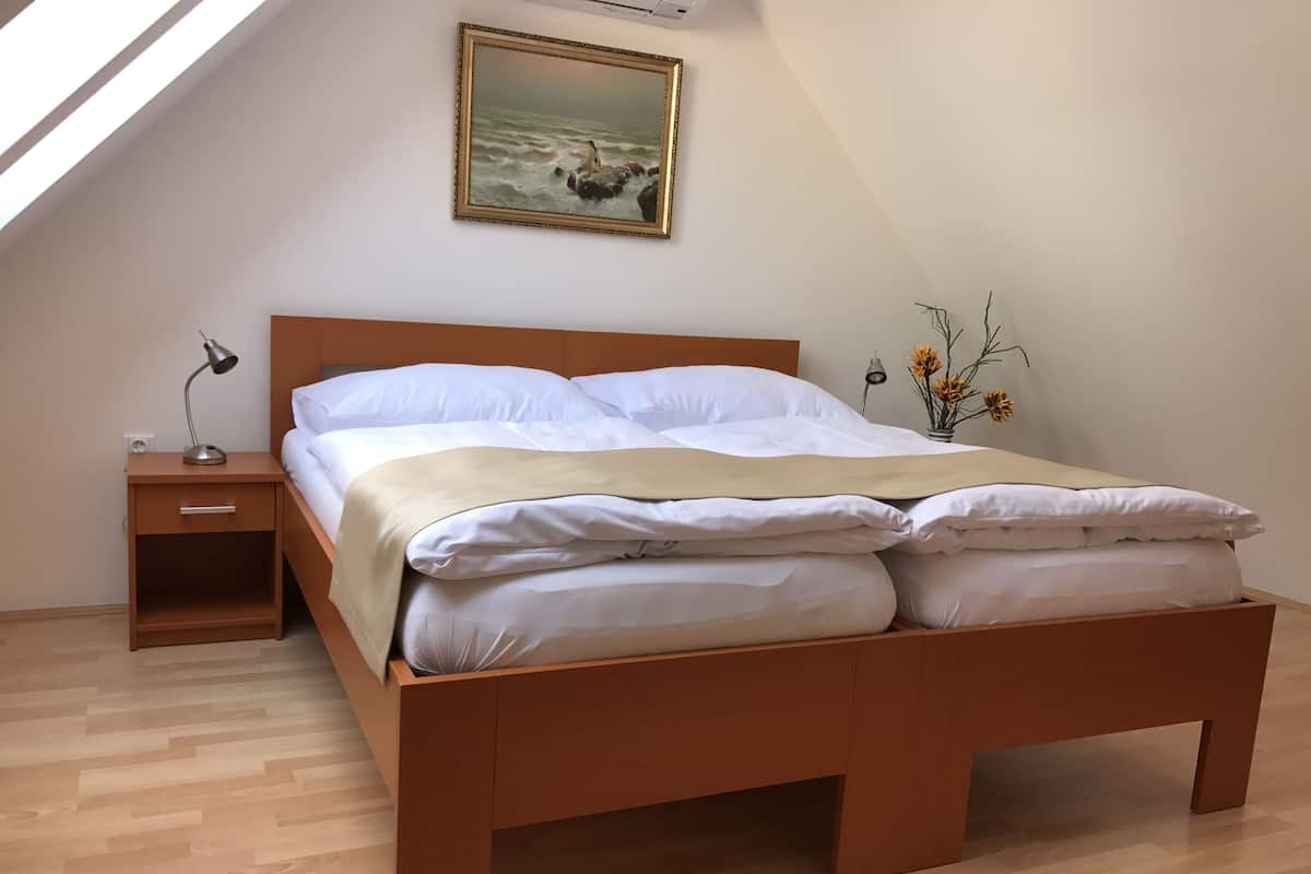 A bedroom with a wooden bed, a nightstand, a lamp, a painting, and a vase with flowers.