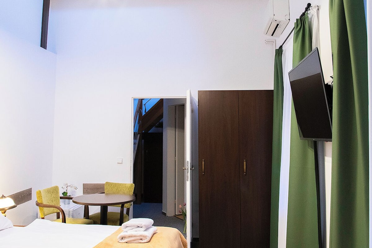 A hotel room with a bed, a desk, a chair, a TV, and a door leading to another room.