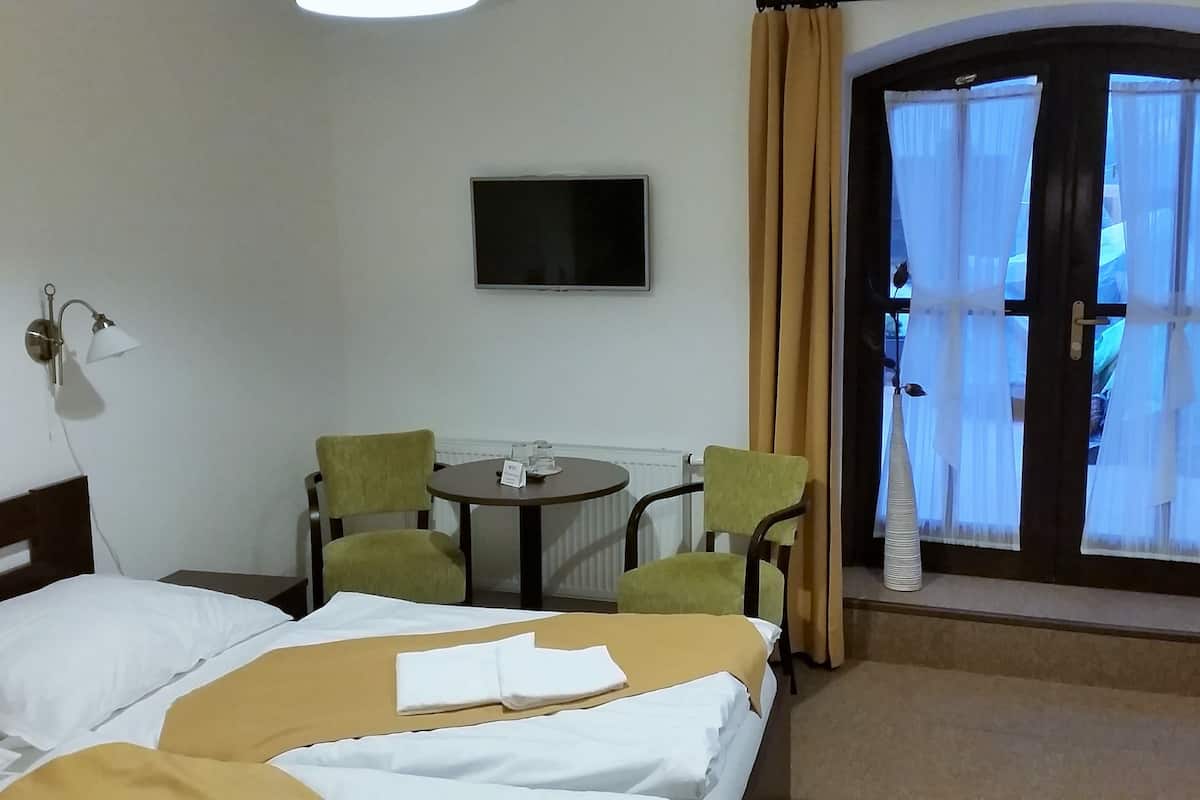 A hotel room with a bed, two chairs, a small table, a TV, and a window with curtains.