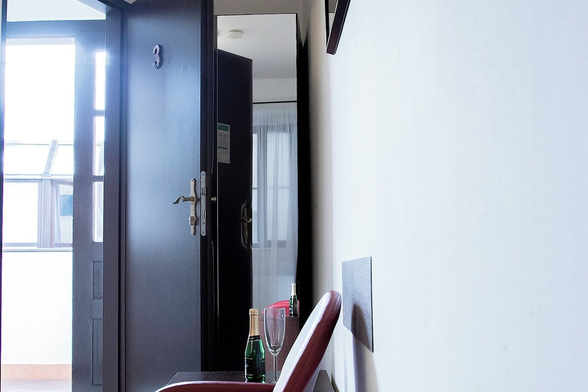 A room with a dining table set for two, a door leading to an outdoor area, and a wall-mounted television.