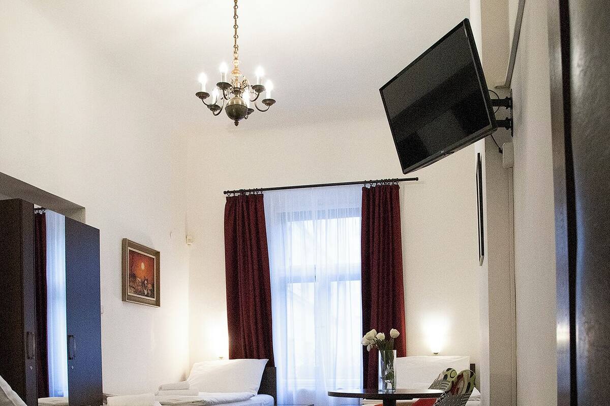 A hotel room with two beds, a desk, a TV mounted on the wall, and a small table with a vase of flowers.