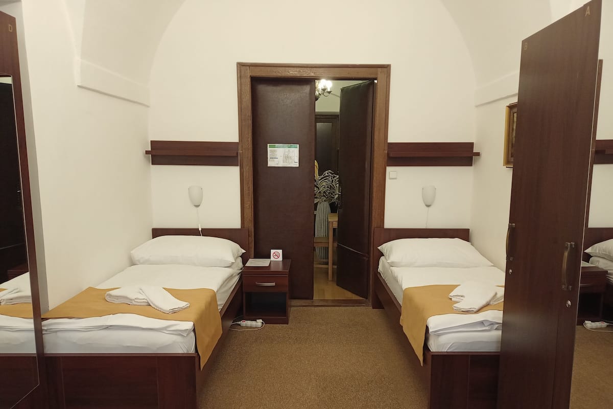A hotel room with two single beds, a wooden headboard, a nightstand with a phone, and a door leading to a bathroom.