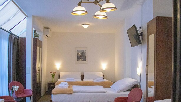A hotel room with two beds, a sitting area with a chair, a desk, a mirror, and a ceiling light fixture. - Old Prague House (Prague)