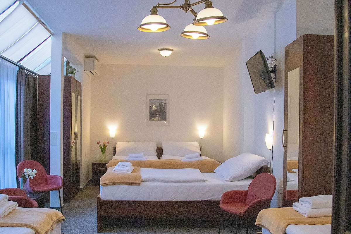 A hotel room with two beds, a sitting area with a chair, a desk, a mirror, and a ceiling light fixture.