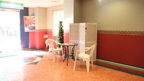 A room with a red and beige color scheme, featuring two white chairs, a small table, and a potted plant. - Hotel TROPICAL OSAKA - Adults Only (Osaka)