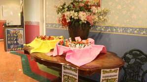 A reception desk with a vase of flowers, a sign, and a table with a yellow cloth. - Hotel TROPICAL OSAKA - Adults Only (Osaka)