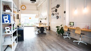 A modern office space with a wooden table, white chairs, and a bookshelf. - Movylodge Hostel (Bangkok)