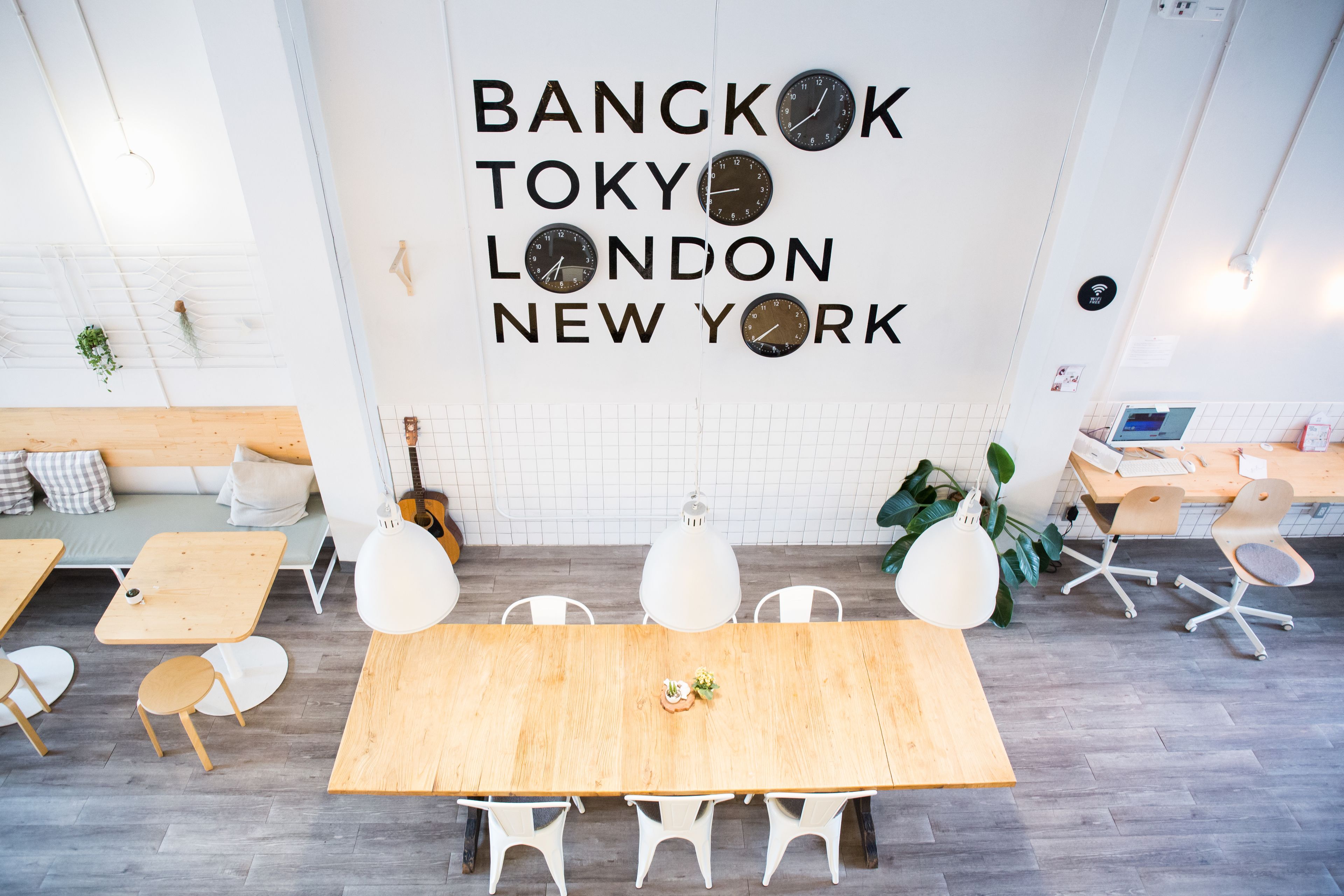 Ein modernes Interieur mit einem Holzes Esstisch, weißen Stühlen und einer Wand, die Uhren für Bangkok, Tokio, London und New York zeigt.