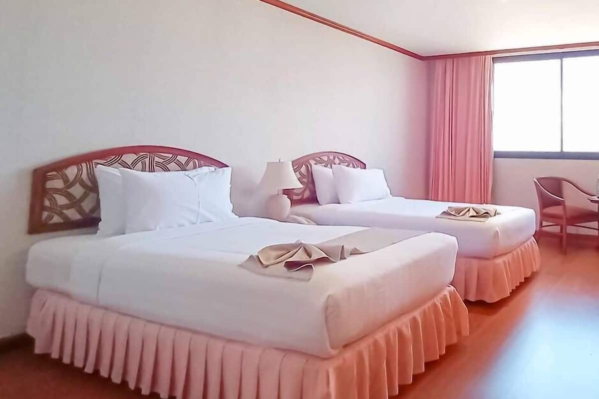 A hotel room with two beds, a window with curtains, a chair, and a wooden floor.