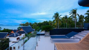 A rooftop terrace with a view of the sea, palm trees, and traditional buildings. - AQUA Villas Rawai (Rawai)