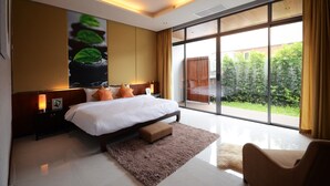 A modern bedroom with a large bed, a nightstand, a bedside lamp, a window with curtains, and a view of greenery outside. - AQUA Villas Rawai (Rawai)