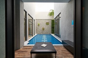 A modern indoor pool area with stone walls, glass doors, and a wooden table in the foreground. - Villa ballet (Taichung)