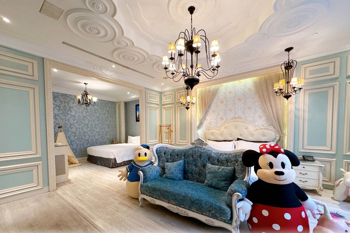 A luxurious hotel room with a large bed, a blue sofa, and a Mickey Mouse plush toy.