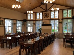 A spacious dining area with multiple tables and chairs, large windows with curtains, and a ceiling fan. - Champs Yazuh B&B (Jiji)