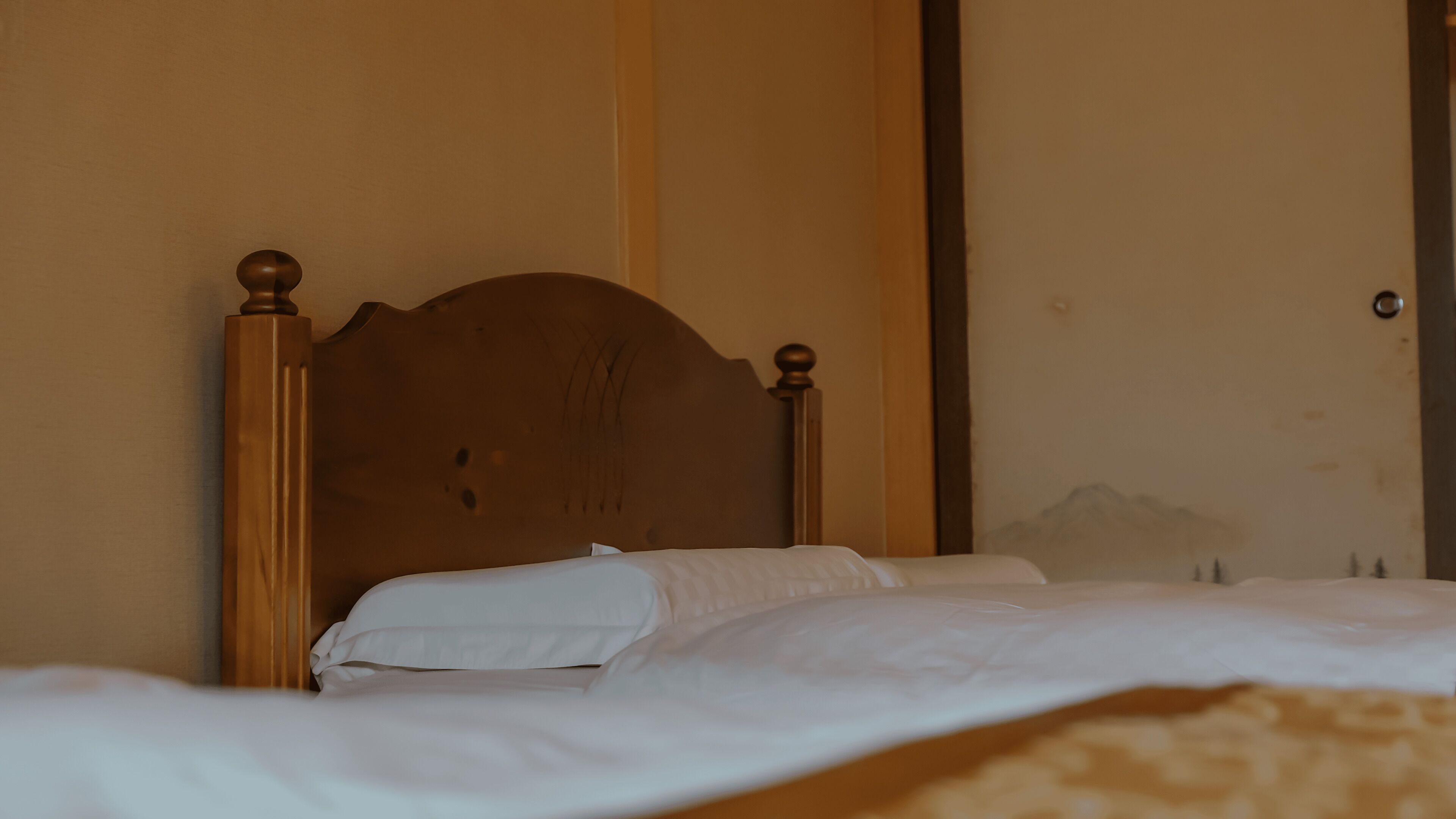 A bed with a wooden headboard, white bedding, and a patterned blanket.