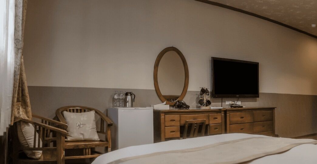 A bedroom with a bed, a wooden dresser, a mirror, a television, and a chair.