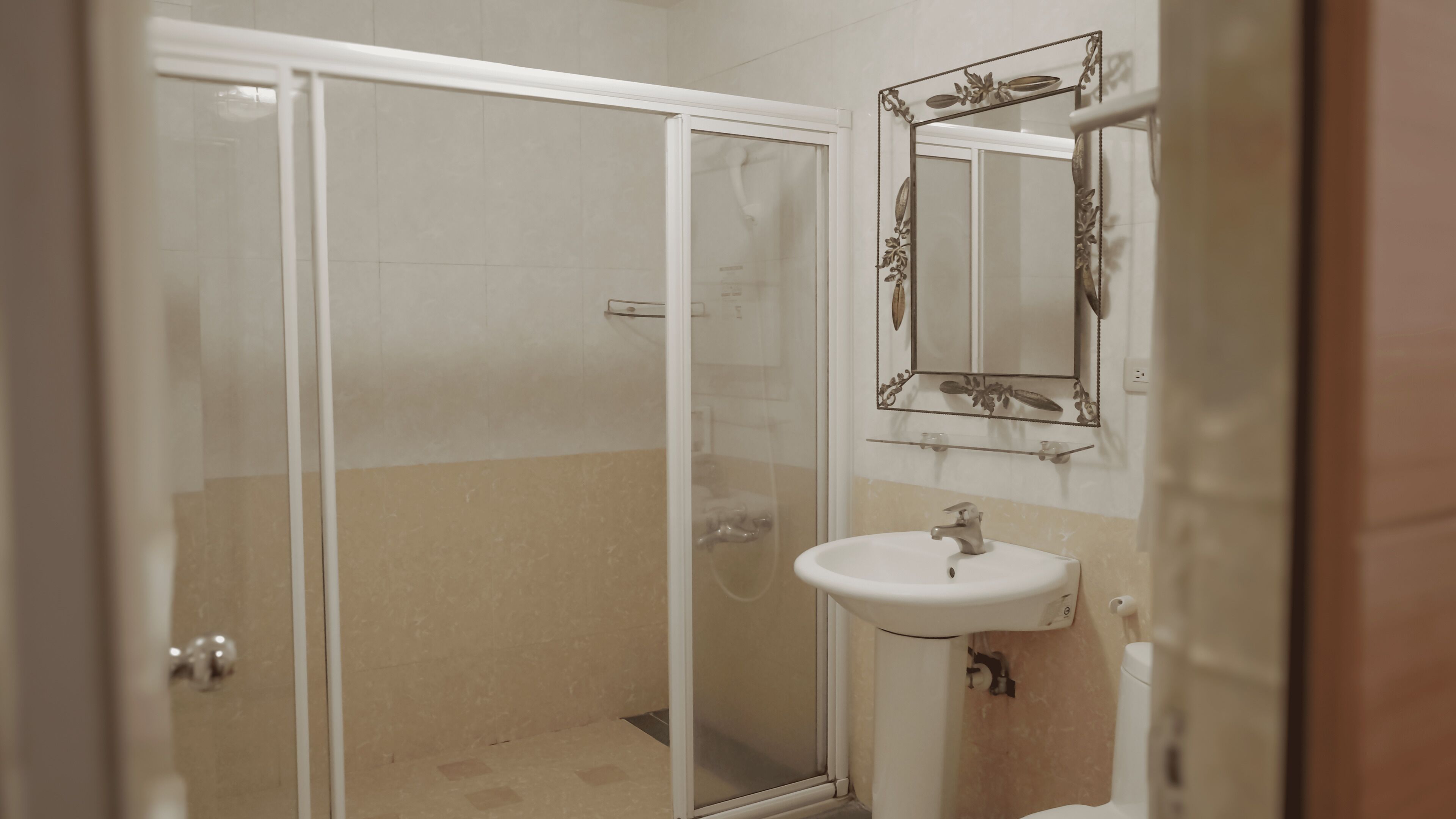 A bathroom with a glass shower enclosure, a sink, and a decorative mirror.