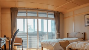 Een hotelkamer met een groot raam, een bed, een bureau en een stoel.