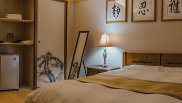 A hotel room with a bed, a television, a refrigerator, and framed calligraphy on the wall.