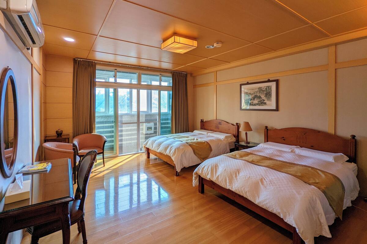 A hotel room with two beds, a desk, a chair, and a large window.