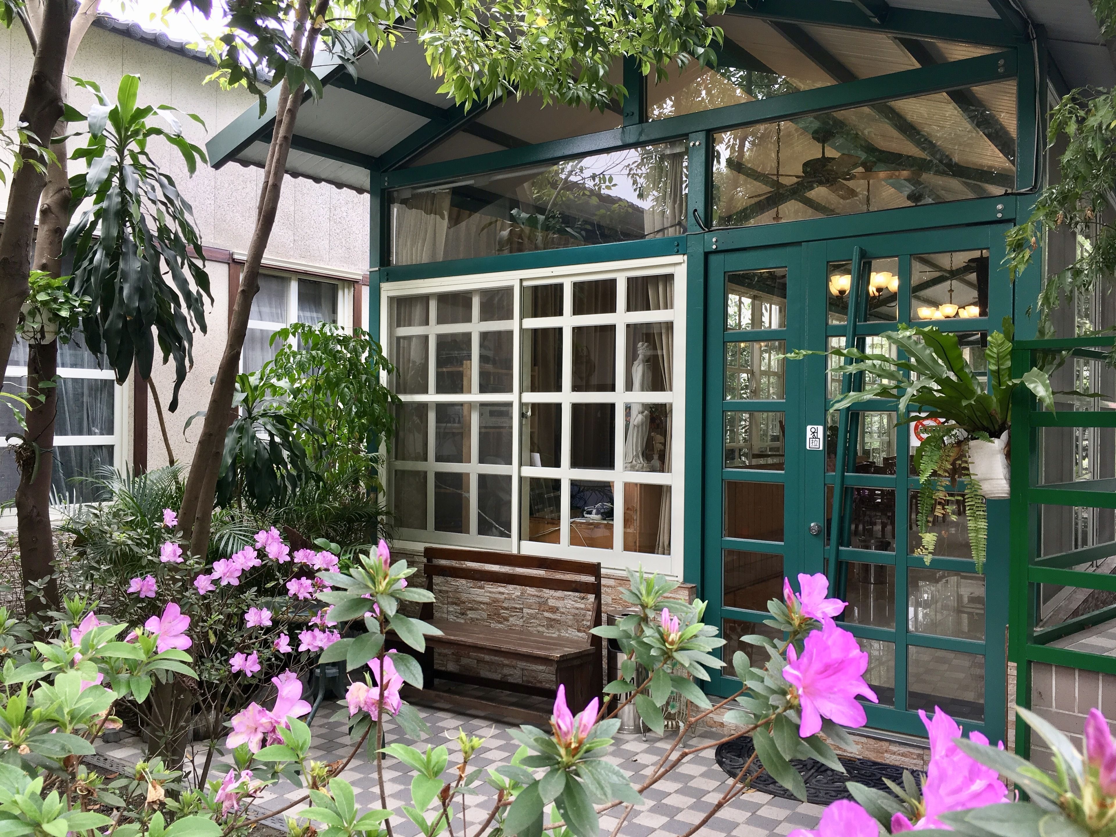 A conservatory with a bench, potted plants, and a view of the interior through large windows.
