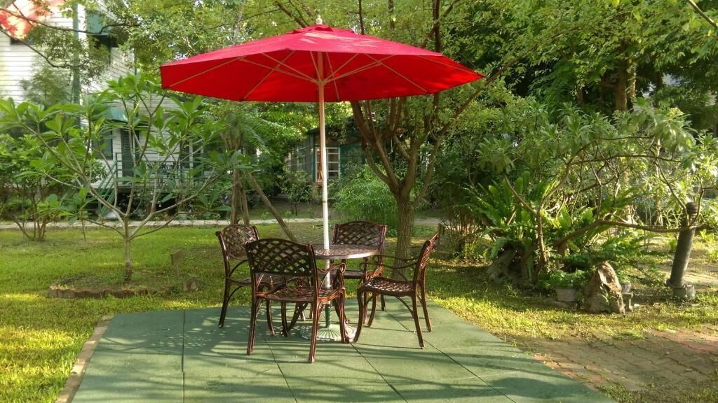 A patio with a table and chairs, a red umbrella, and surrounding greenery.