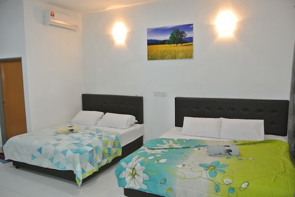 Two single beds with headboards, a wall-mounted air conditioner, and a framed picture of a field with a tree.