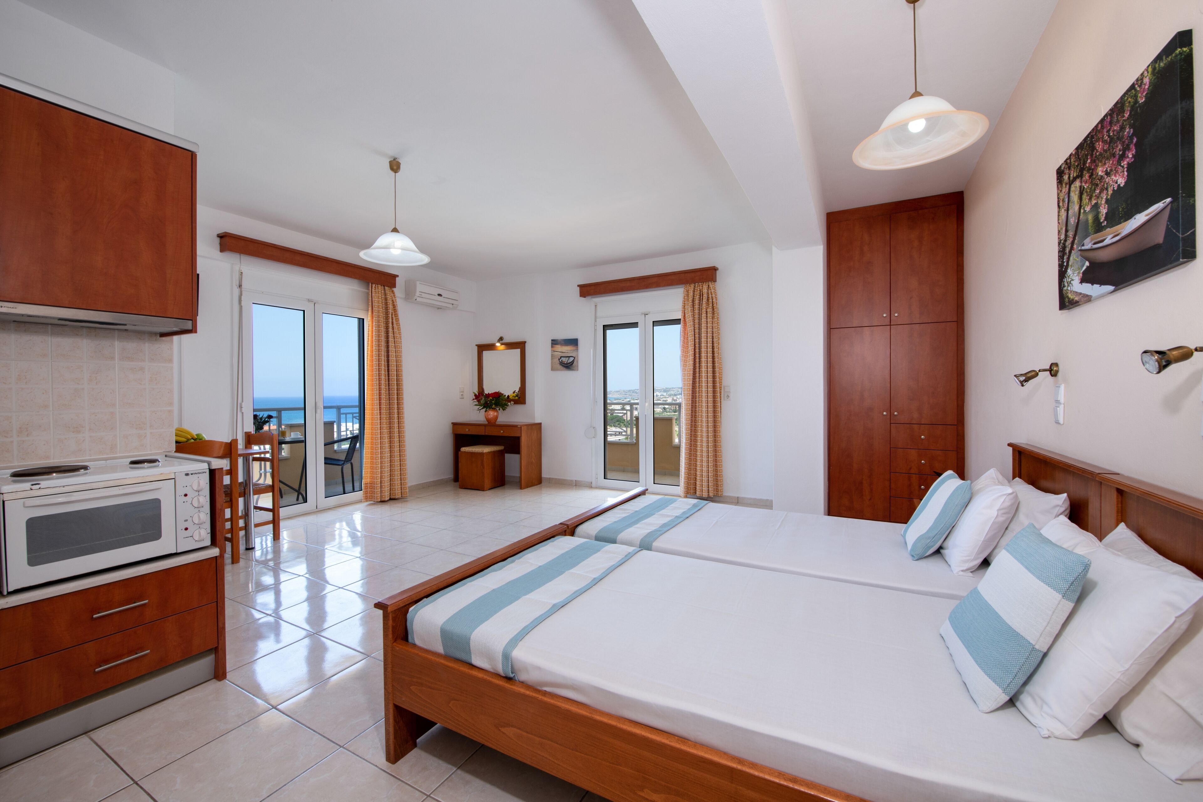 A hotel room with a bed, a kitchenette, a dining area, and a view of the sea.