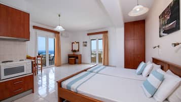 Habitación de hotel con cama, kitchenette, comedor y vista al mar.
