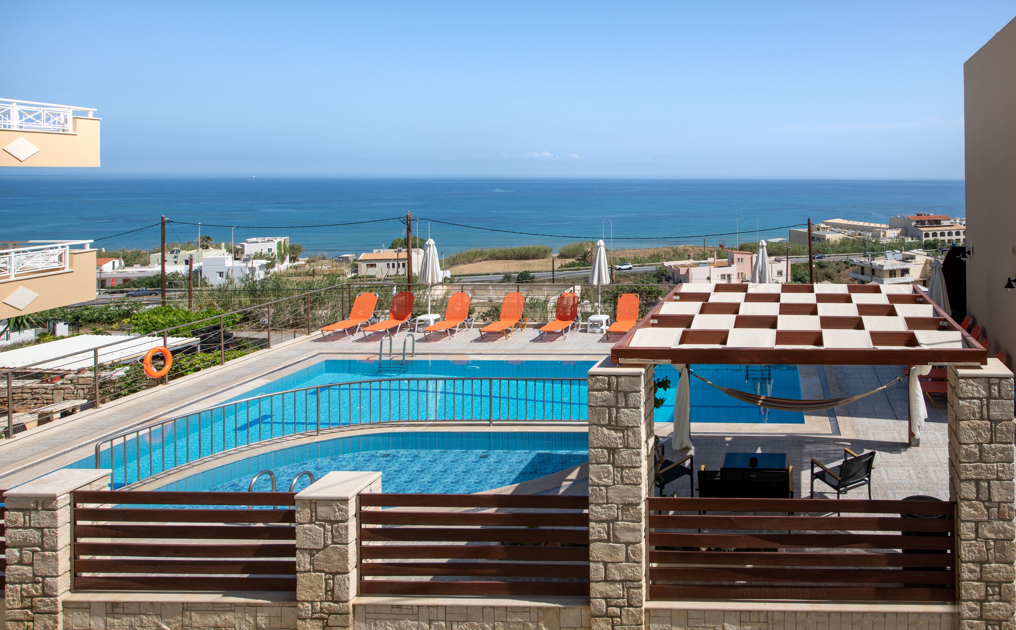 Une piscine sur le toit, avec des chaises longues orange et une vue sur la mer.