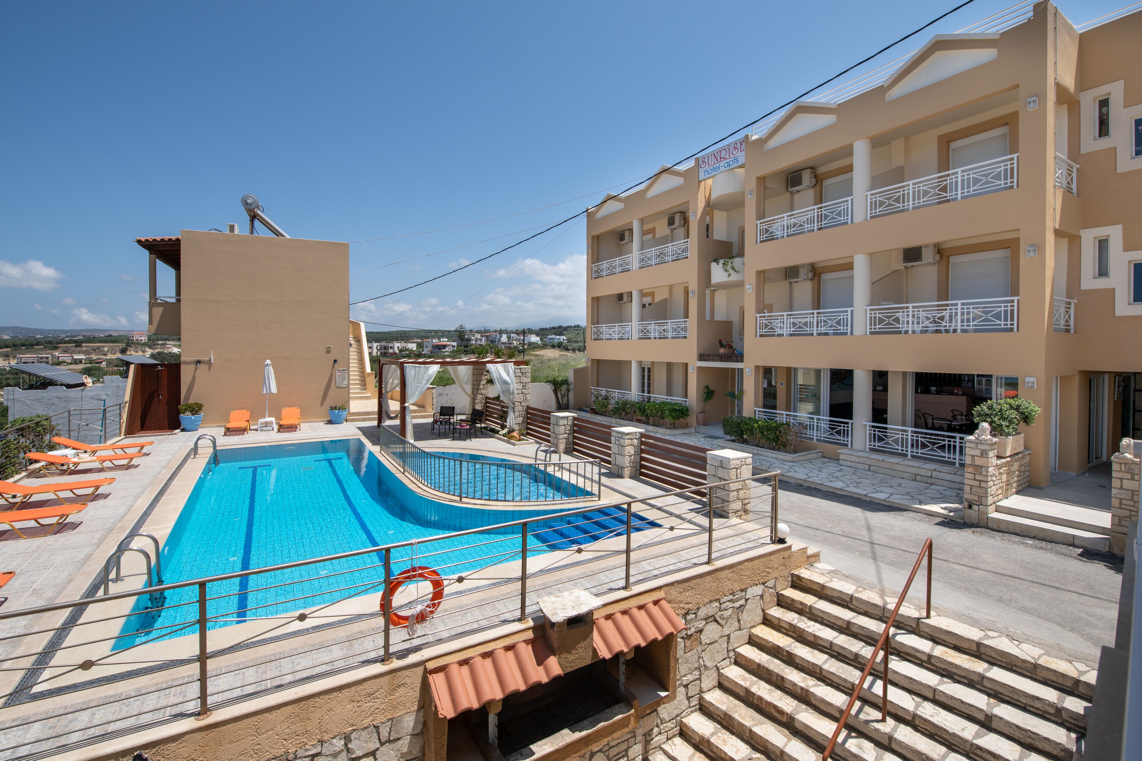A hotel with a swimming pool, outdoor seating, and a view of the surrounding landscape.