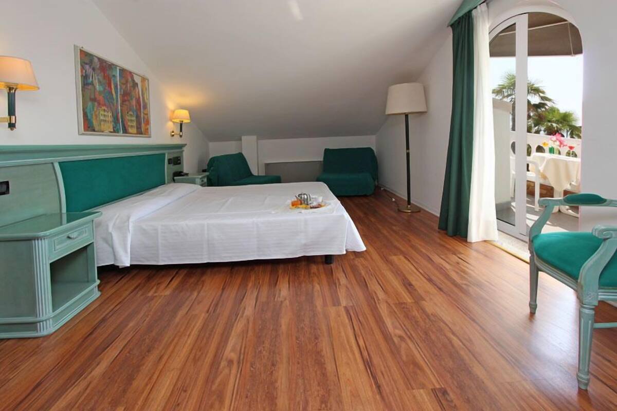A hotel room with a bed, two chairs, a desk, and a balcony with a view.