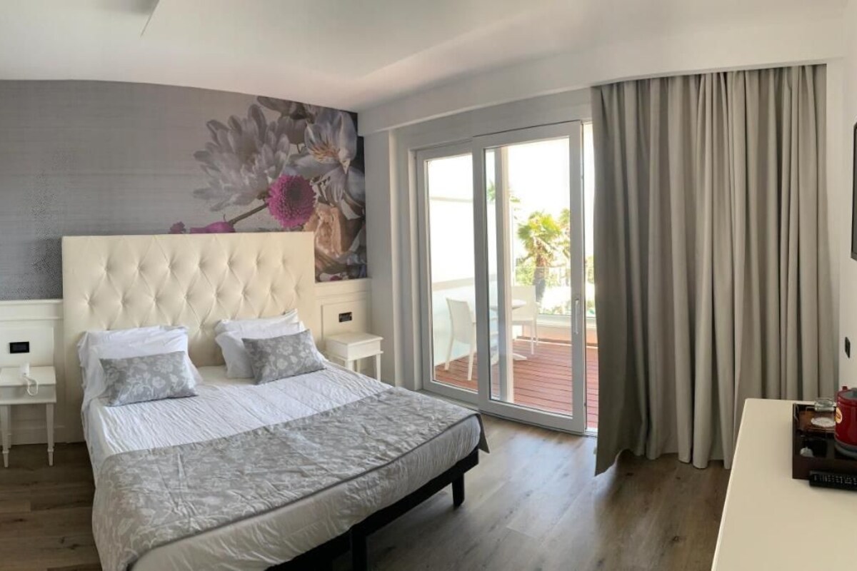 A bedroom with a large bed, a headboard, a nightstand, a TV, and a view of the outdoors.