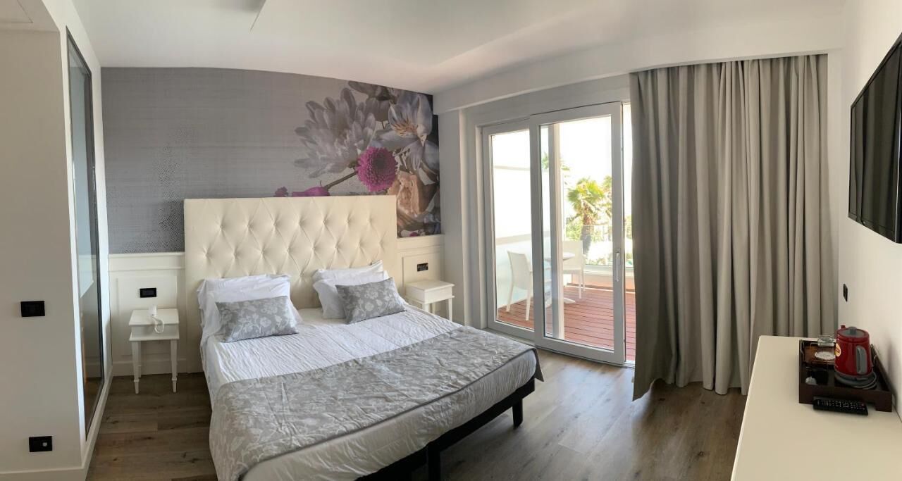A bedroom with a large bed, a sliding glass door to a balcony, a flat-screen TV, and a small bedside table.
