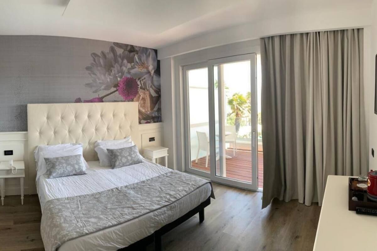 A bedroom with a large bed, a headboard, a nightstand, a TV, and a view of the outdoors.
