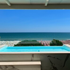 A pool with a view of the ocean and beach umbrellas. - Park Hotel Cellini (Jesolo)