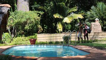 A swimming pool with a brick border, surrounded by lush greenery and a stone wall.