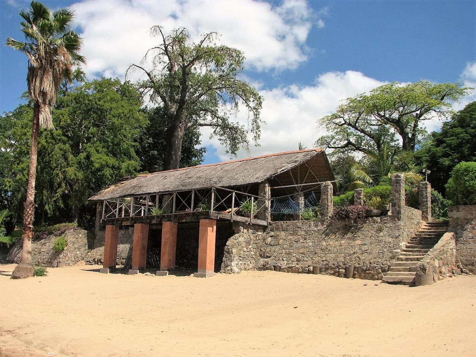 A rustic building with a thatched roof, stone walls, and a wooden staircase leading up to it.
