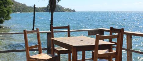 Een houten terras met een tafel en stoelen, uitkijkend op een wateroppervlak.