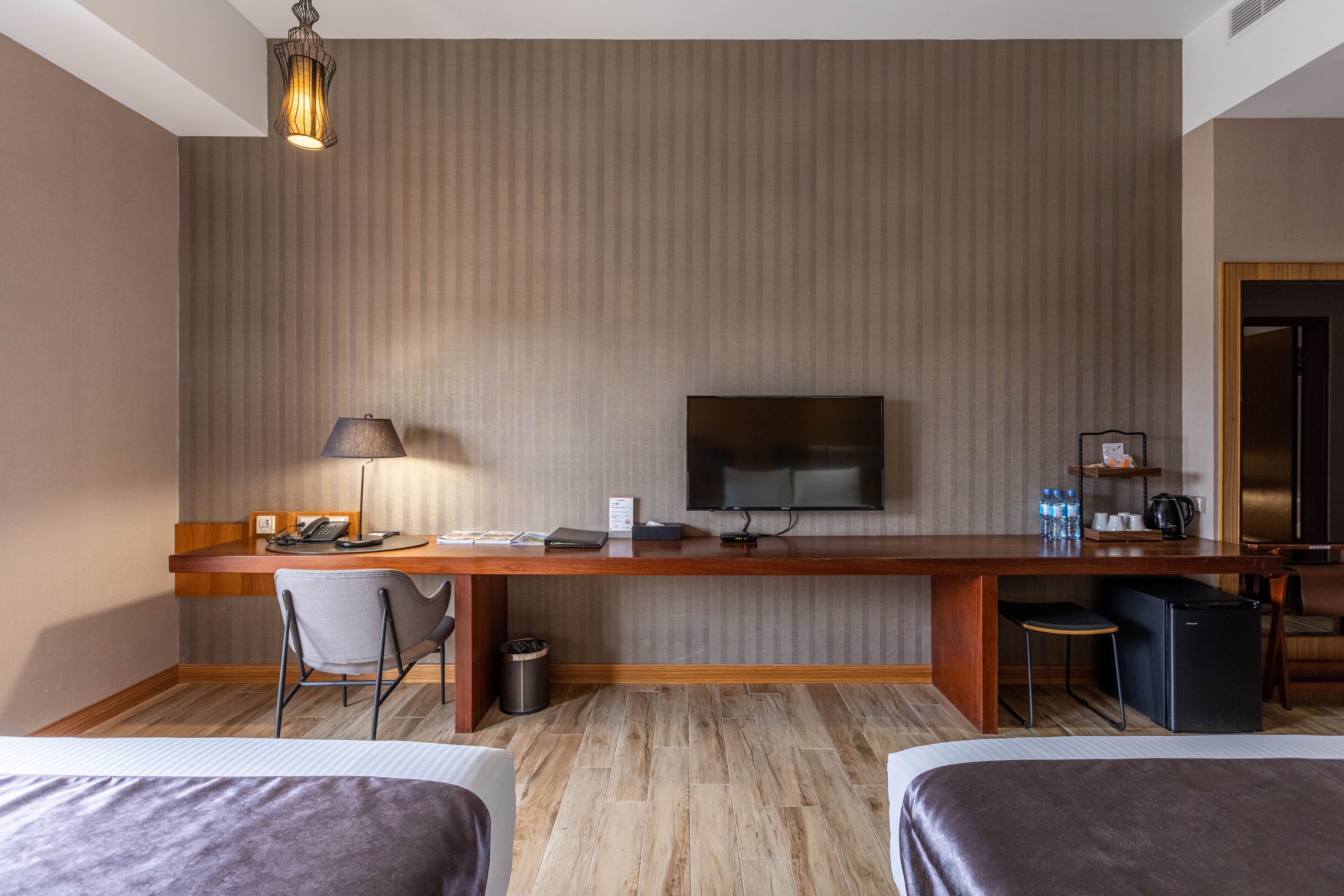 Une chambre d’hôtel avec un bureau en bois, une télévision, une chaise, un lit et une poubelle.