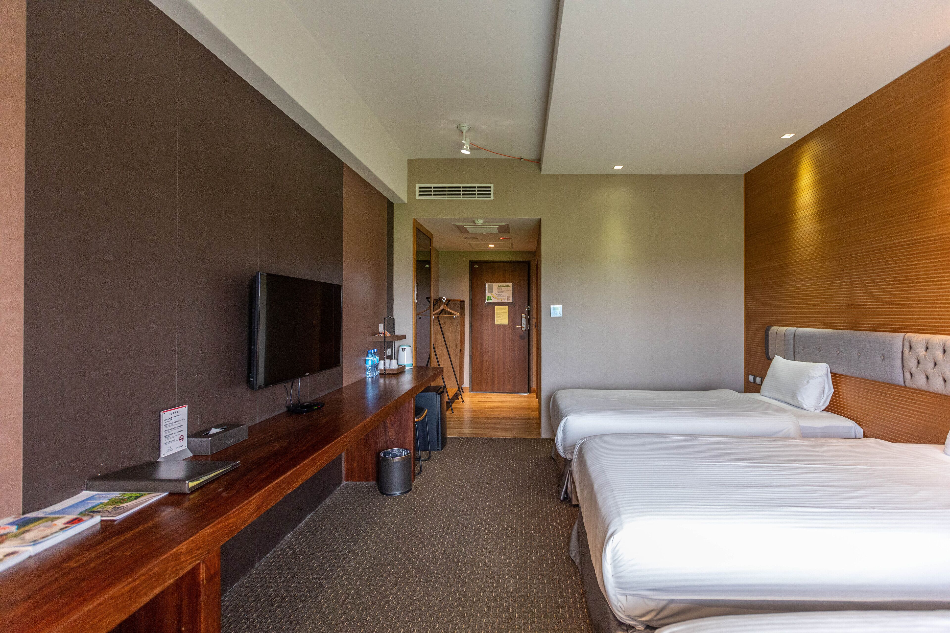 Habitación de hotel con escritorio de madera, televisor de pantalla plana, dos camas, piso alfombrado y cabecero de madera.