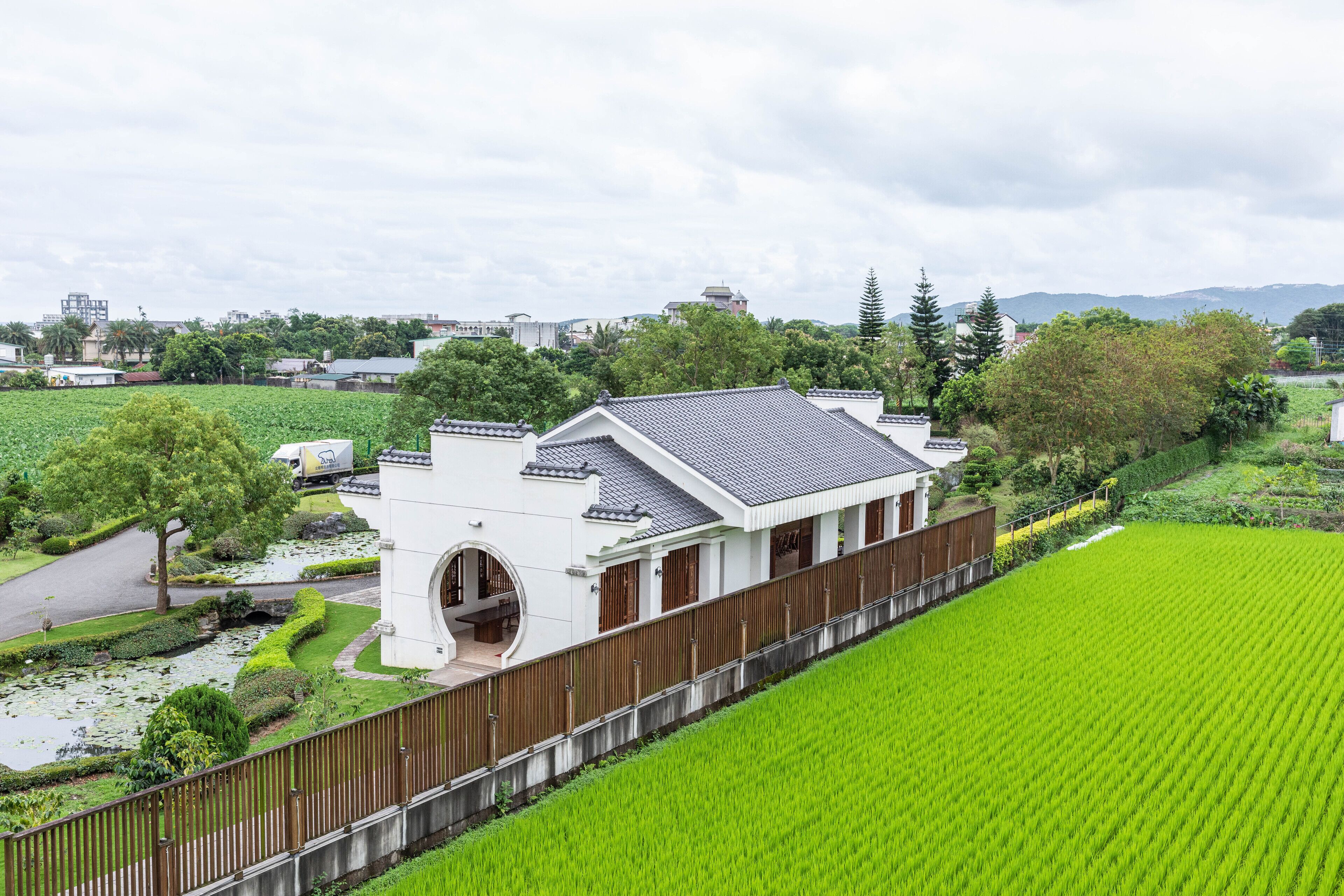 A traditional Japanese house with a curved roof, surrounded by lush green fields and a wooden fence.